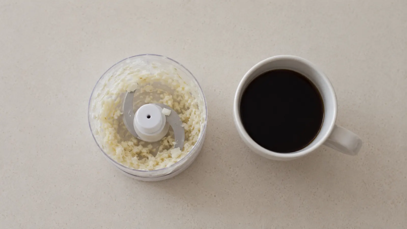 Mini food processor next to a measuring cup showing the 3-cup capacity compared to a standard coffee mug