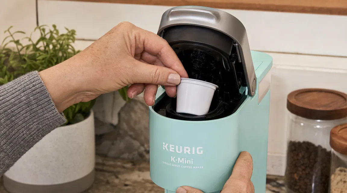 Hand inserting a K-Cup pod into the Keurig K-Mini brew chamber